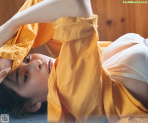 A woman sitting on a window sill wearing a yellow shirt.