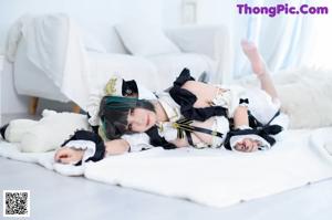 A woman in a maid outfit sitting on a bed.