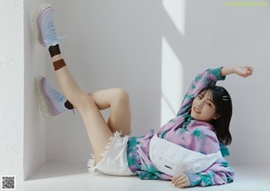 A woman in a pink and green tie dye shirt is posing for a magazine.