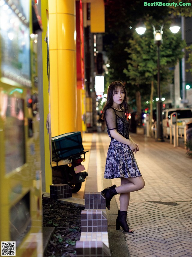 A woman in a dress and boots standing on a sidewalk.