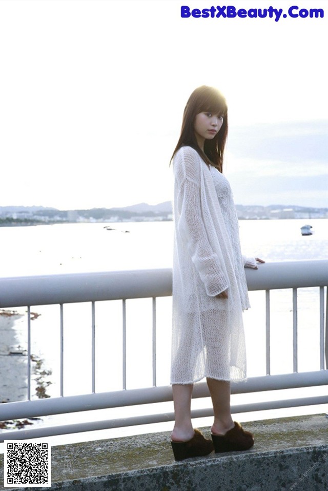 A woman standing on a railing by the water.