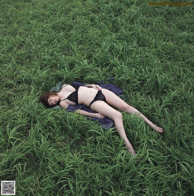 A woman laying in the grass in a black bikini.