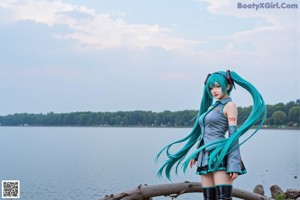 A woman with long blue hair sitting on a rock by the water.