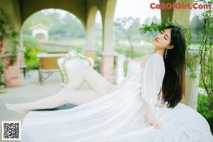 A woman in a white dress sitting on a wooden bench.