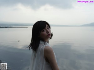 A woman in a white dress sitting on the grass by the water.
