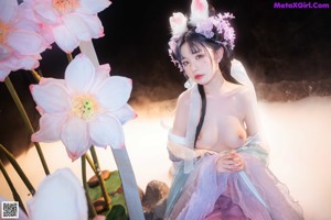 A woman in a pink and blue dress sitting on a rock.