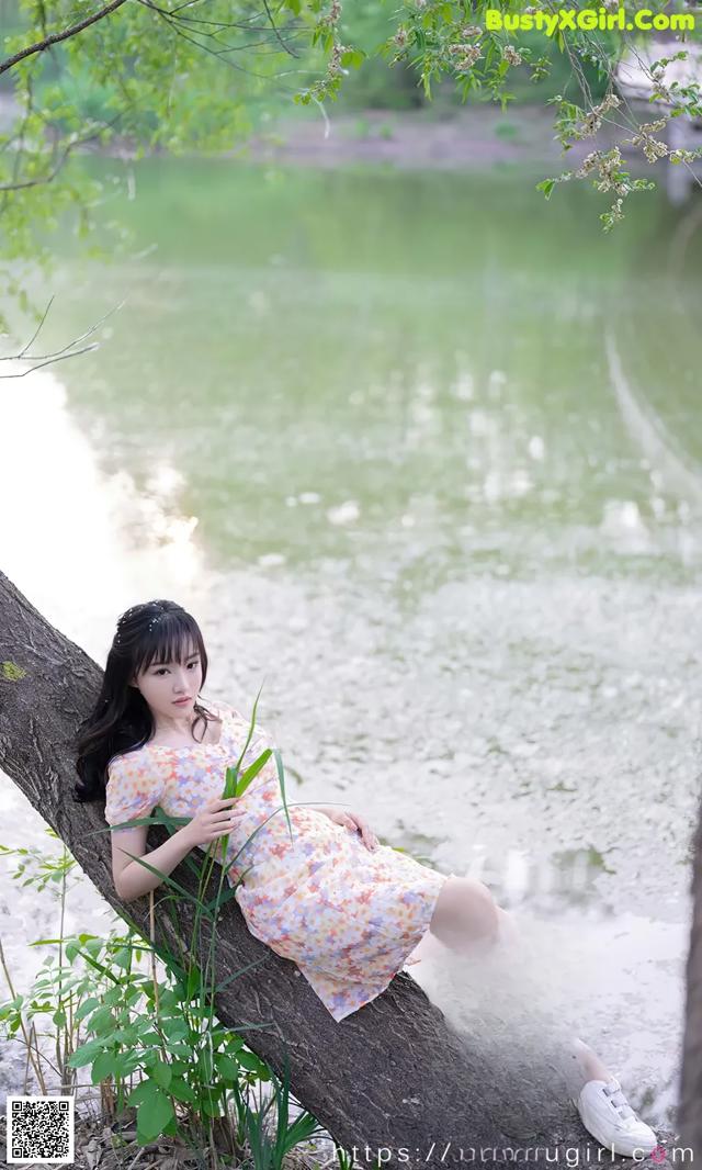 A woman sitting on a tree branch by the water.